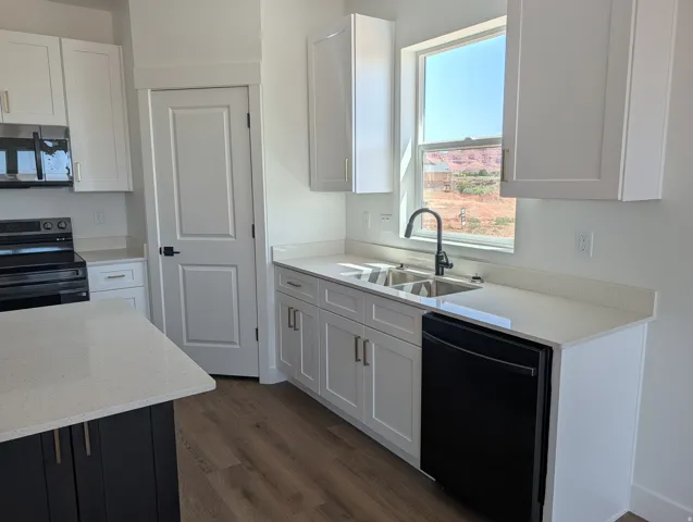 Contemporary kitchen featuring white shaker cabinetry, white countertops, stainless steel double basin sink, black appliances, and wood-finish flooring