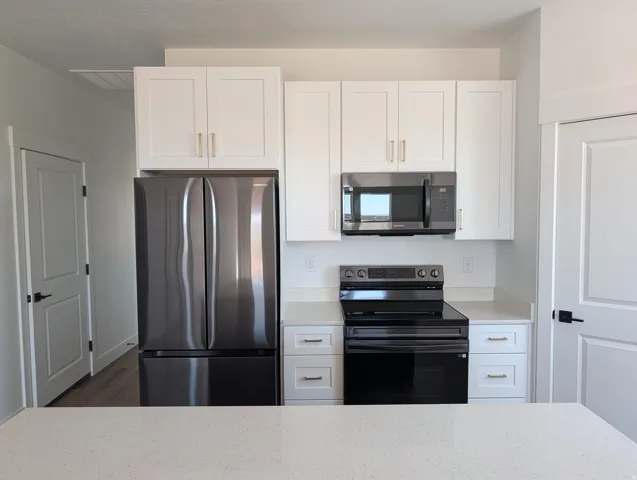 Modern kitchen featuring stainless steel appliances, white shaker cabinetry with gold-finish hardware, a white solid surface countertop, and wood-finish flooring