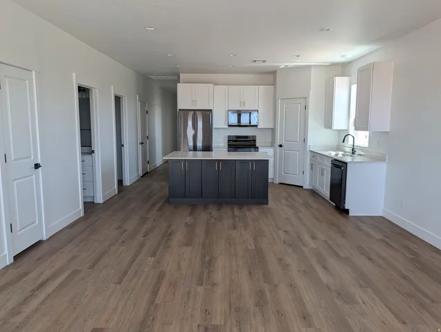 Open-concept kitchen featuring a two-tone island with a light-colored countertop, white cabinetry with dark hardware, stainless steel appliances, and wood-finish flooring