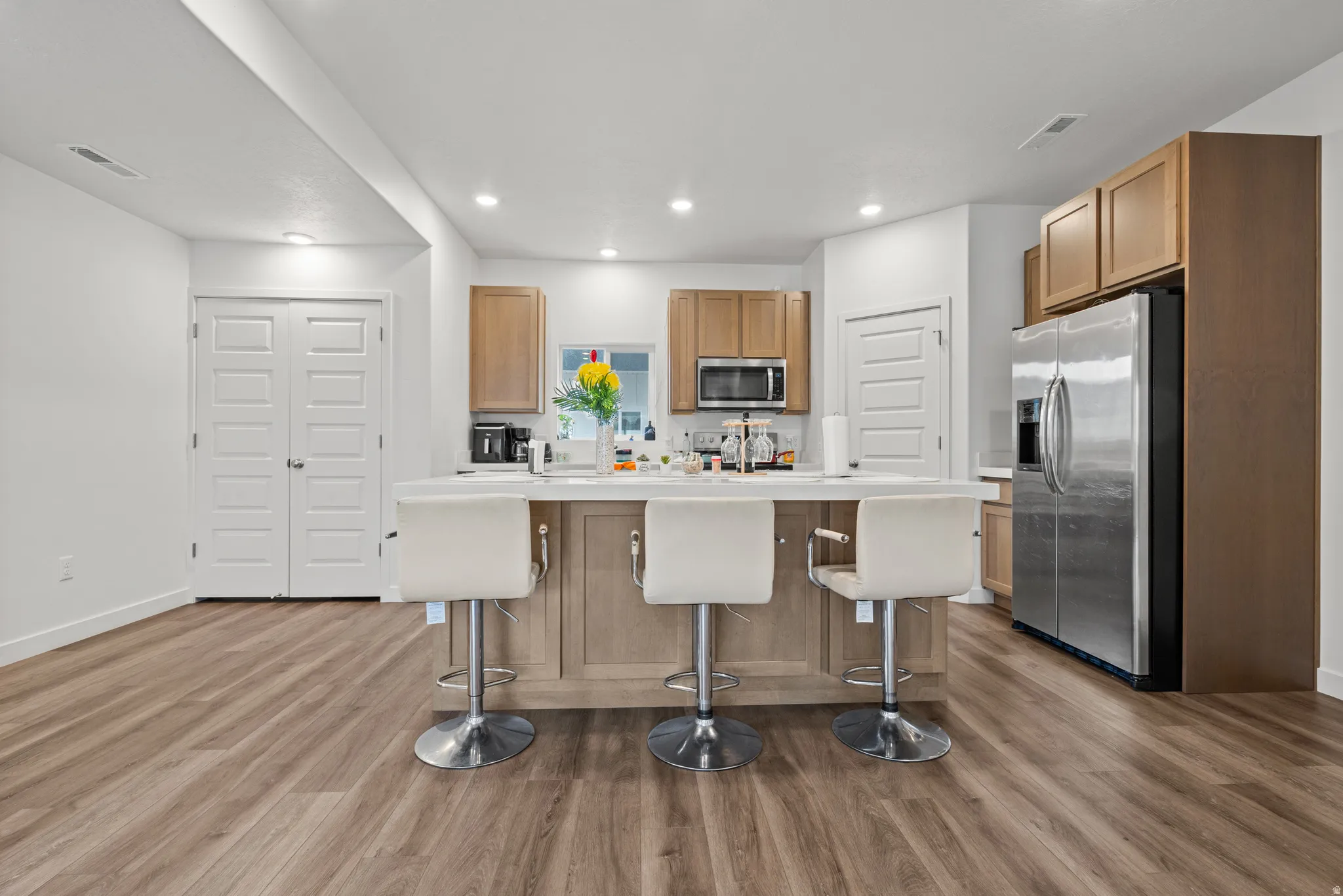 Kitchen with stainless steel appliances, light countertops, a kitchen island, a breakfast bar area, and dark wood-style floors