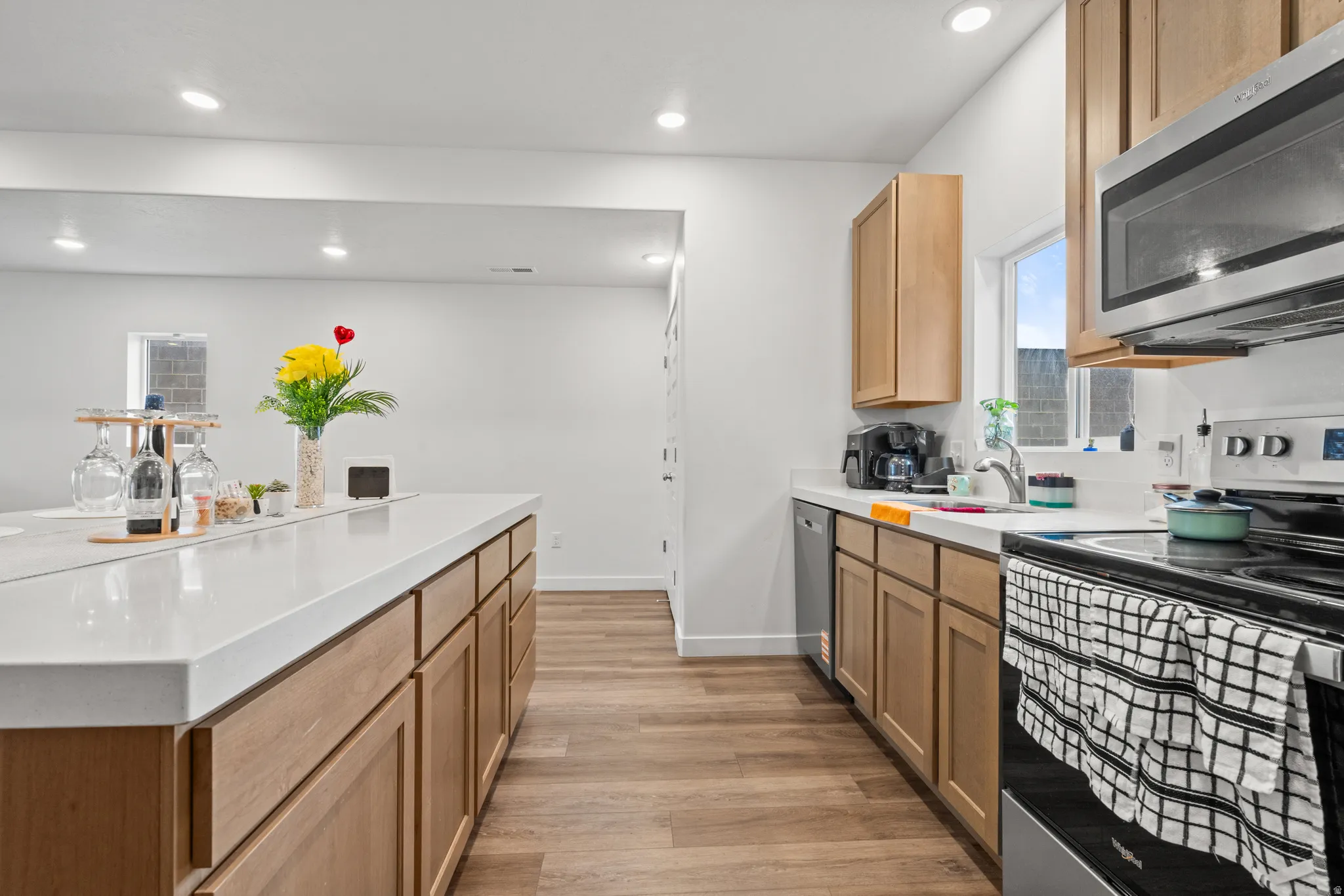 Kitchen with stainless steel appliances, light wood-style flooring, recessed lighting, a kitchen island, and light stone countertops