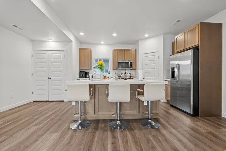 Kitchen with stainless steel appliances, light countertops, a kitchen island, a breakfast bar area, and dark wood-style floors