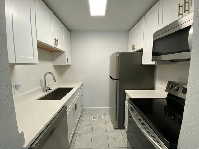 Kitchen featuring stainless steel appliances, white cabinetry, light stone counters, and light marble finish flooring