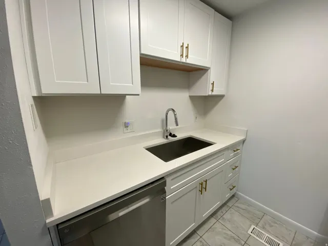 Kitchen featuring stainless steel dishwasher, white cabinetry, light marble finish flooring, and light stone countertops