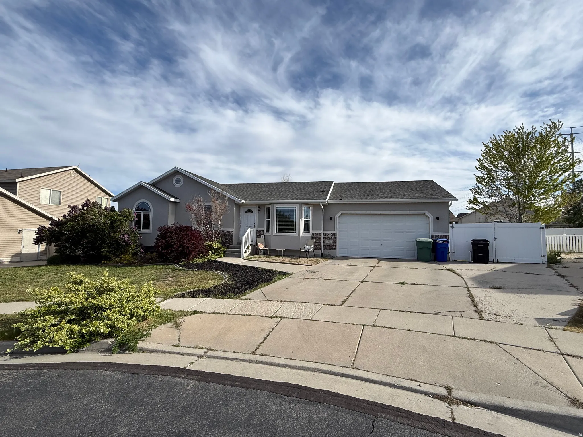 Ranch-style house featuring concrete driveway, an attached garage, stucco siding, a gate, and roof with shingles