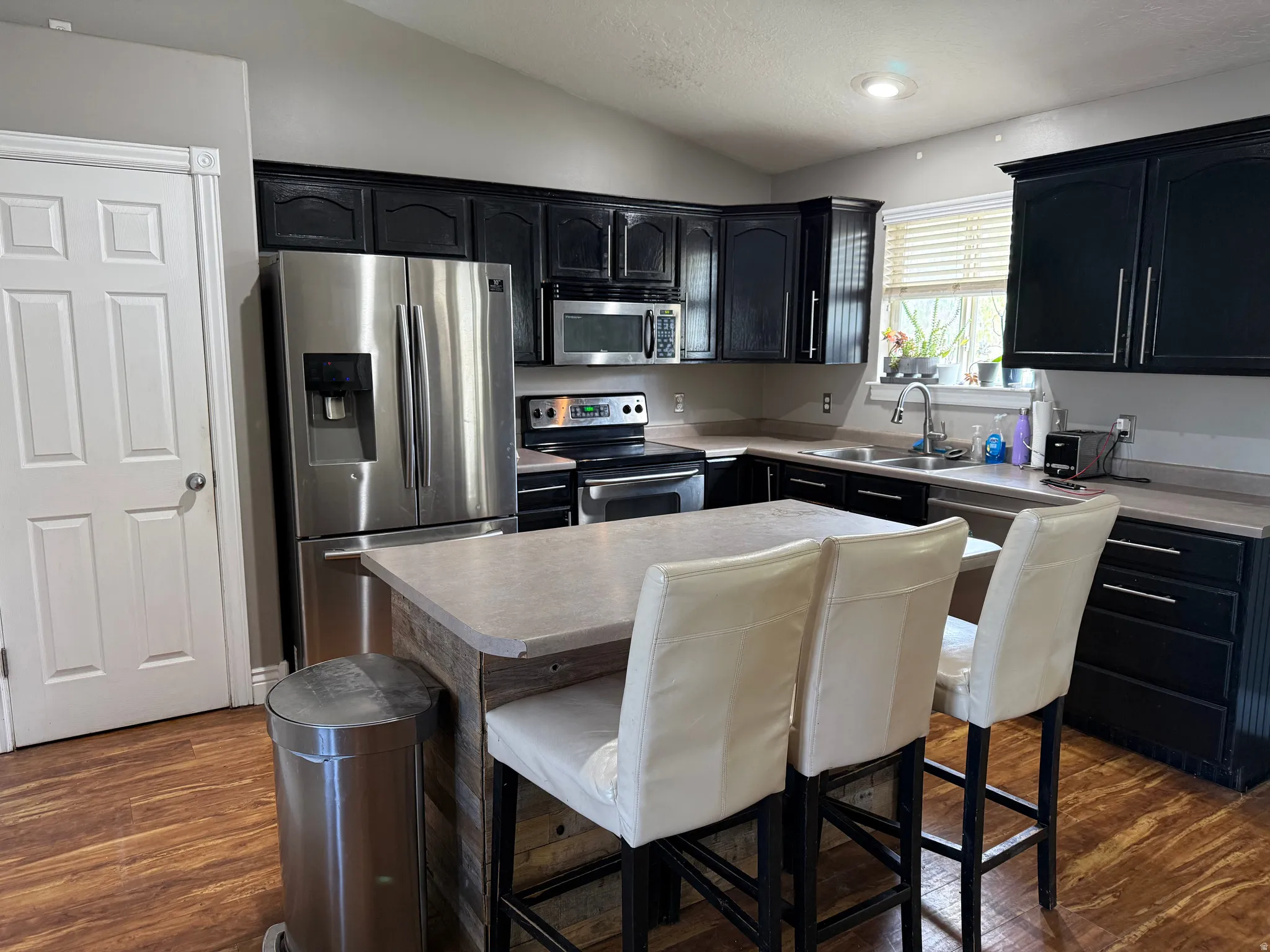 Kitchen with stainless steel appliances, dark cabinetry, a kitchen island, vaulted ceiling, and light countertops