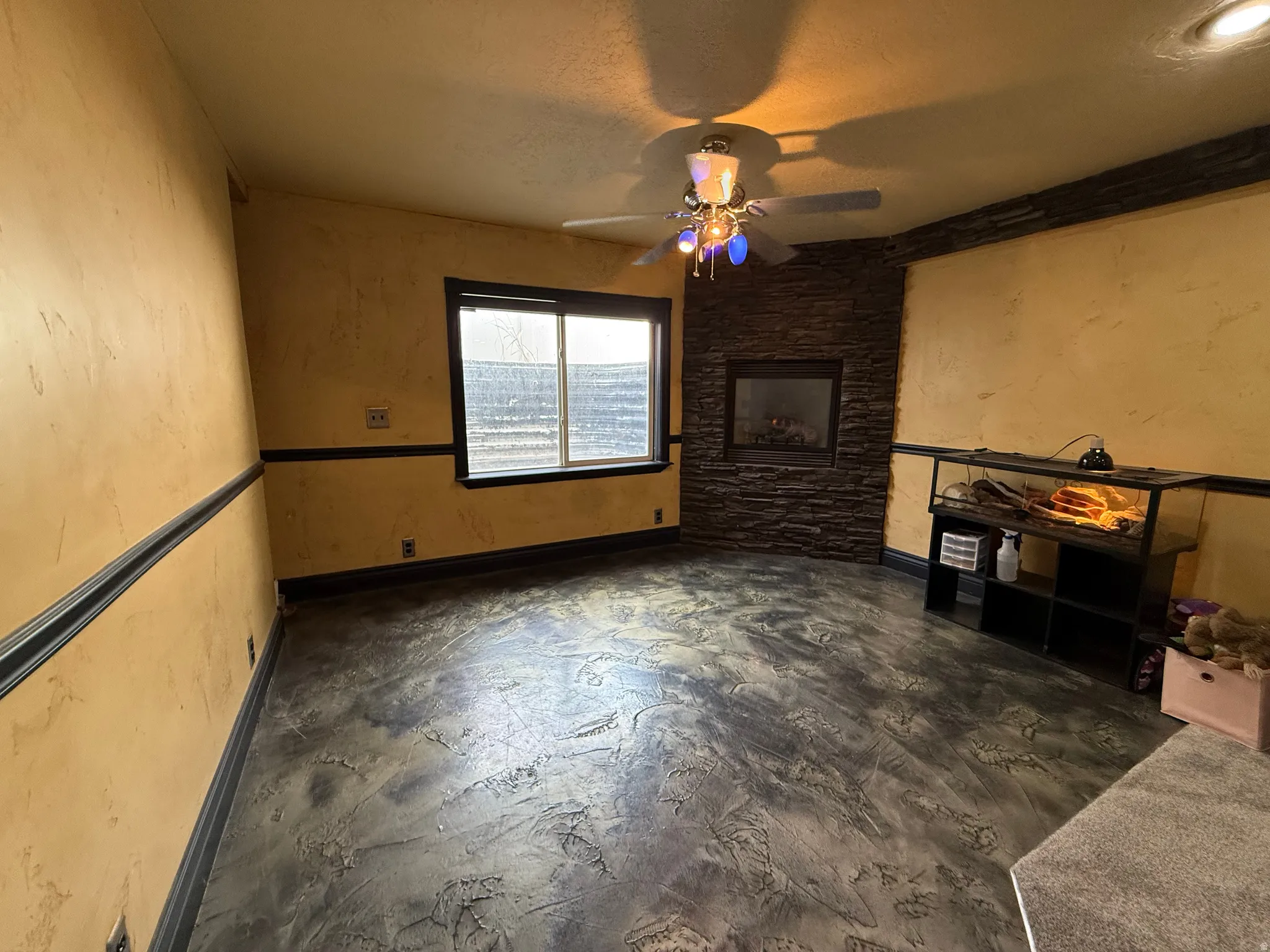 Unfurnished living room with concrete floors, a ceiling fan, and a textured wall