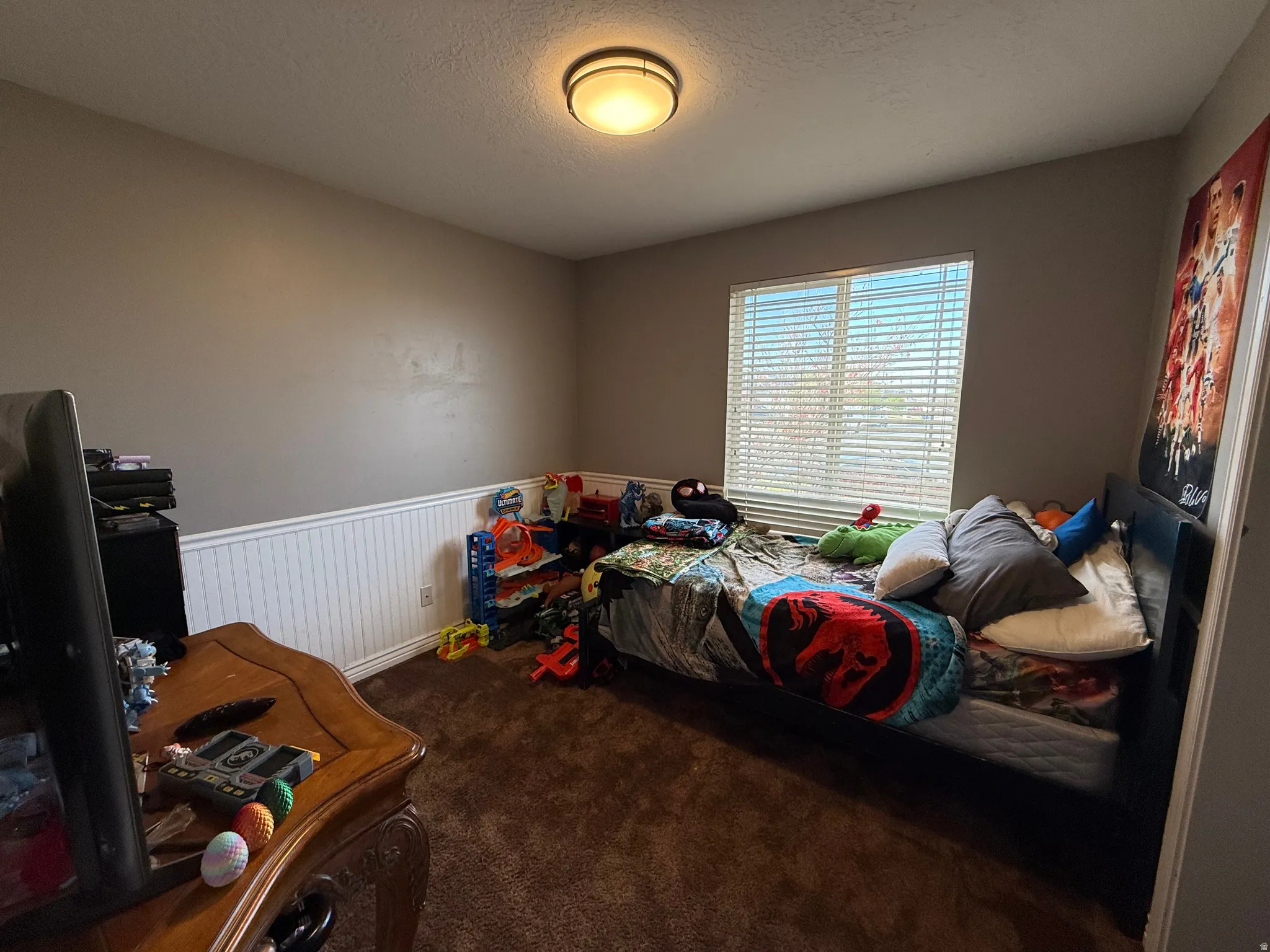 Bedroom featuring wainscoting, dark colored carpet, and a textured ceiling