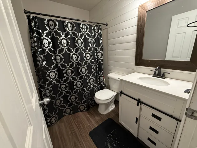 Bathroom featuring vanity, dark wood-style floors, wooden walls, and a shower with curtain