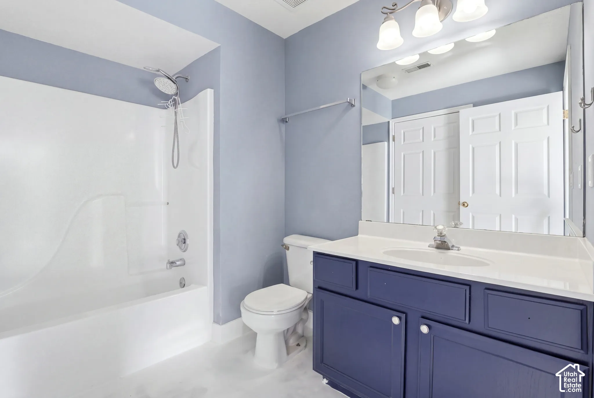 Bathroom featuring a dark-toned vanity, a white composite countertop with an integrated basin, a large wall-mounted mirror, three-light overhead fixture, and a tub-shower combination with a detachable showerhead