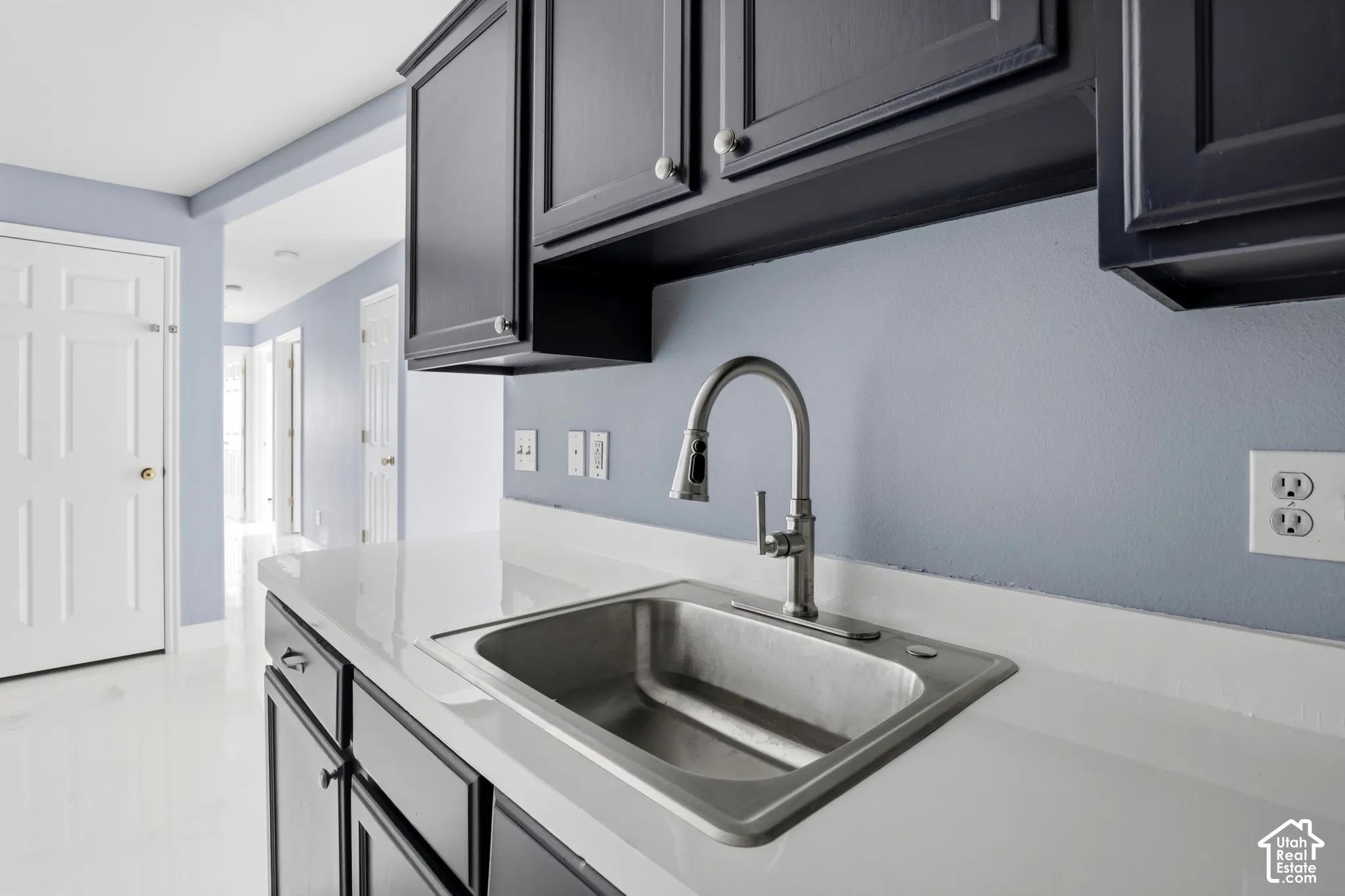 Kitchen featuring dark cabinetry, solid-surface countertops, a stainless steel undermount sink, and a high-arc pull-down faucet
