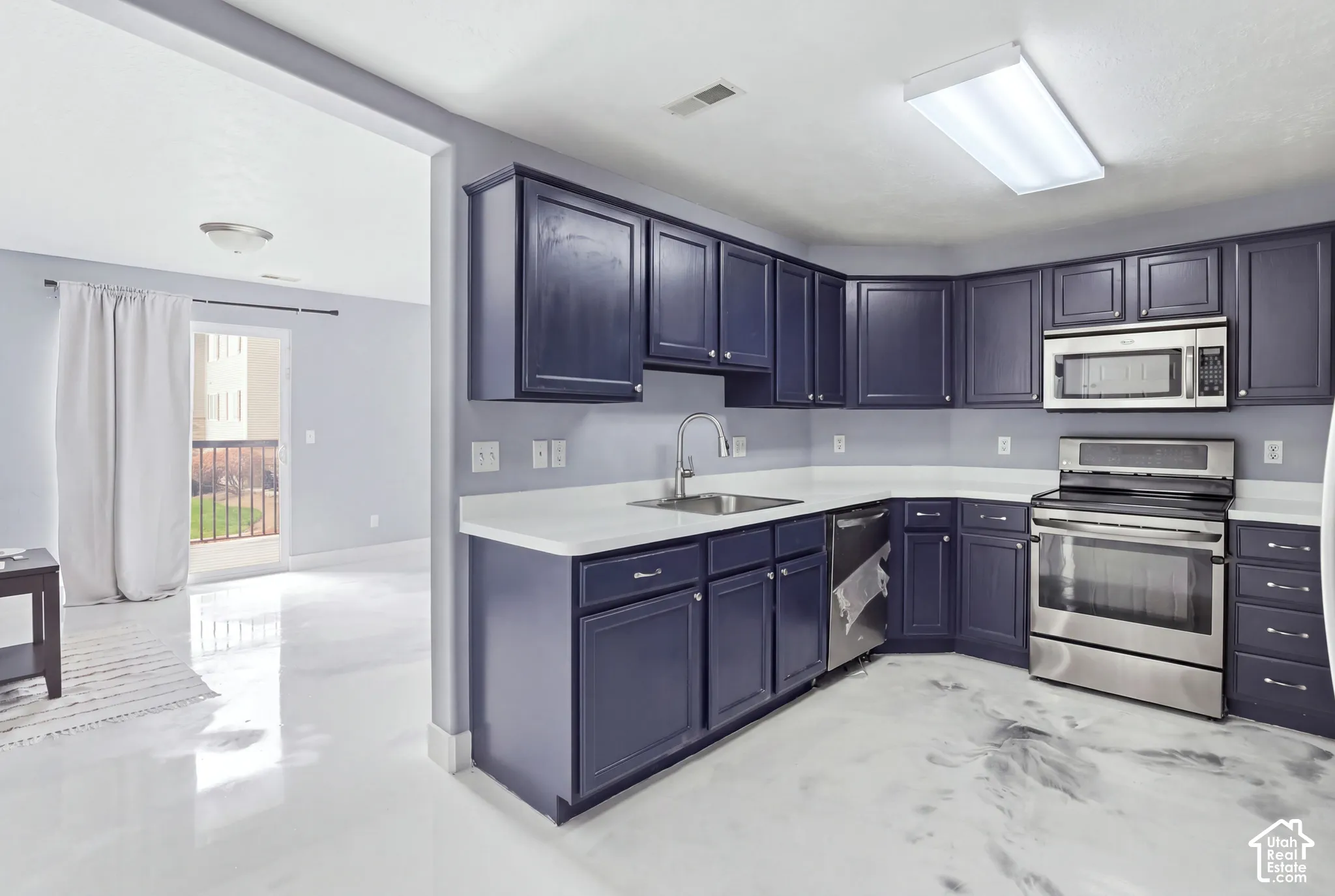 Kitchen featuring deep-toned shaker cabinetry, solid-surface countertops, stainless steel appliances, and high-gloss polished flooring