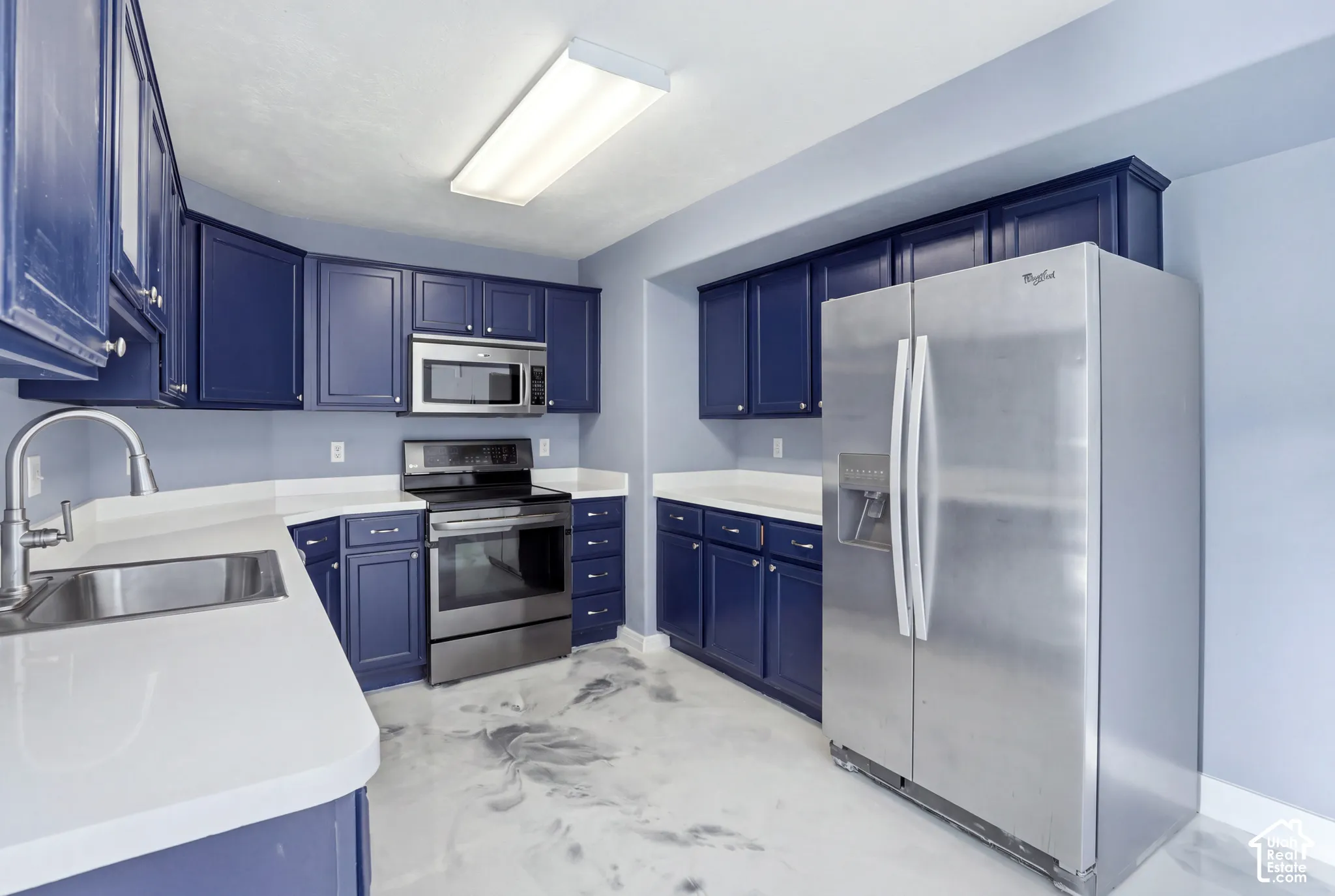 Kitchen featuring navy blue cabinetry, solid surface countertops, stainless steel appliances, and polished decorative flooring