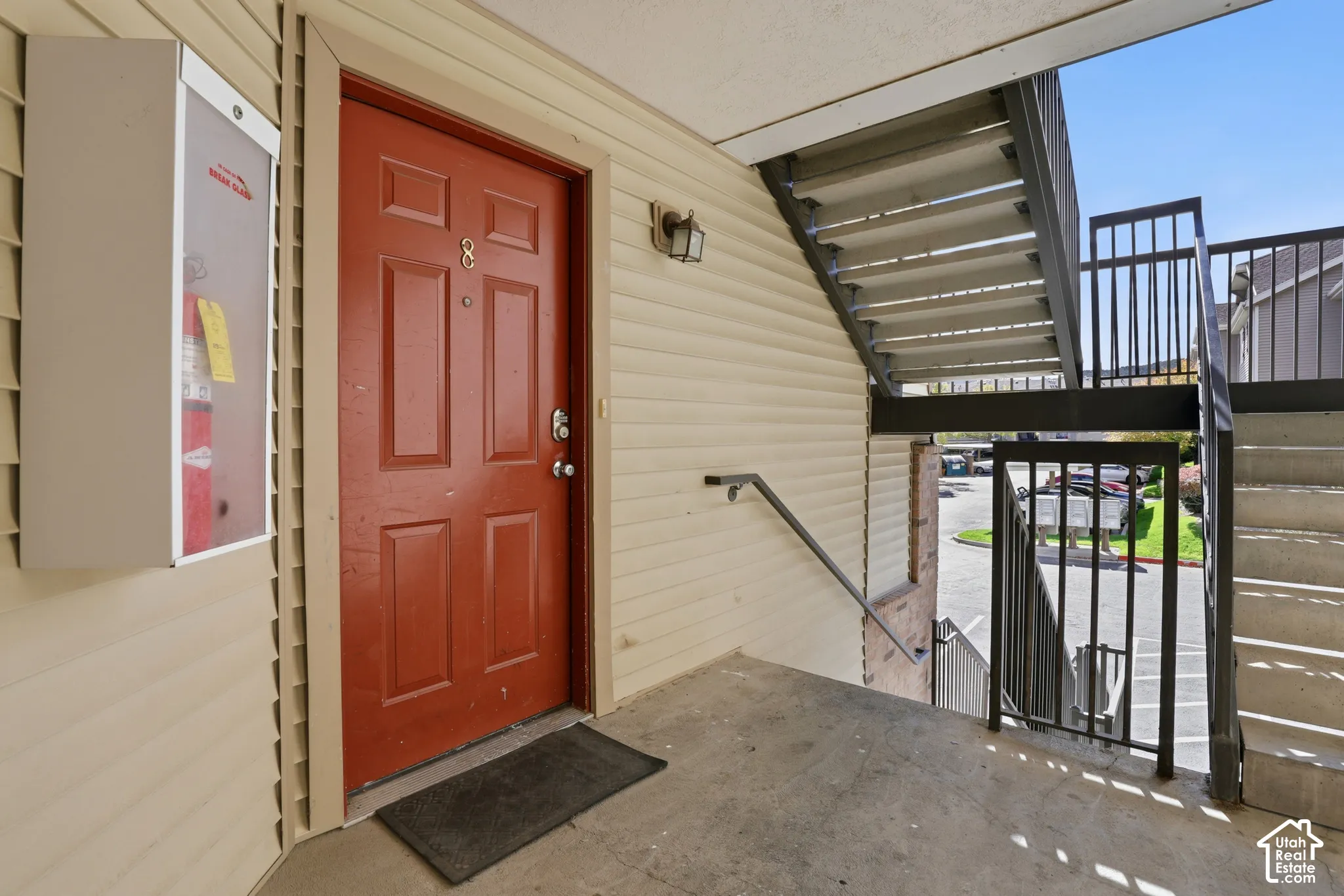 Entryway featuring a six-panel door, neutral vinyl siding, wall-mounted light fixture, and metal stair railing