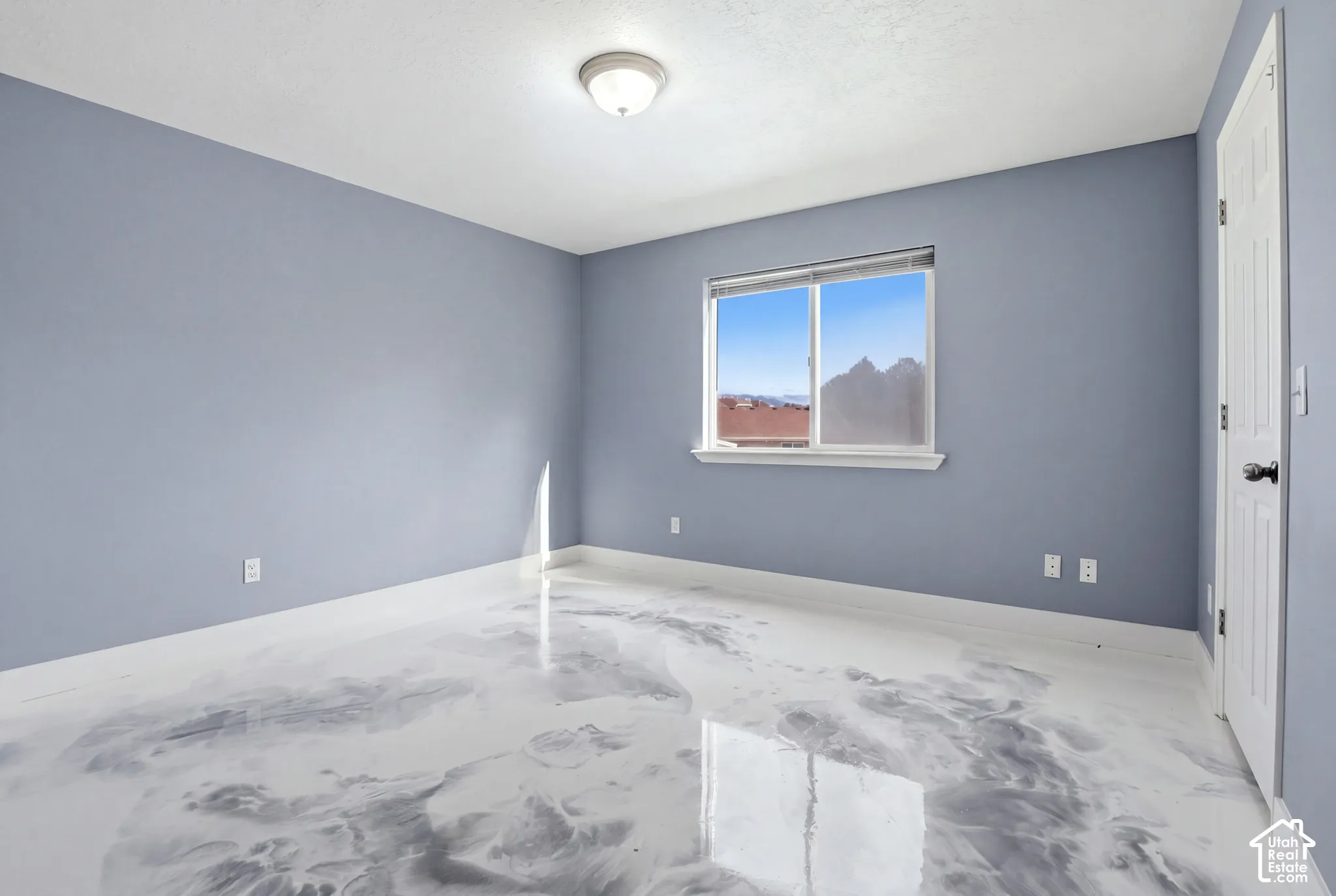 Interior space featuring polished marble-effect epoxy flooring, soft blue wall tones, a single-pane sliding window, a six-panel interior door, and a flush-mount ceiling light fixture