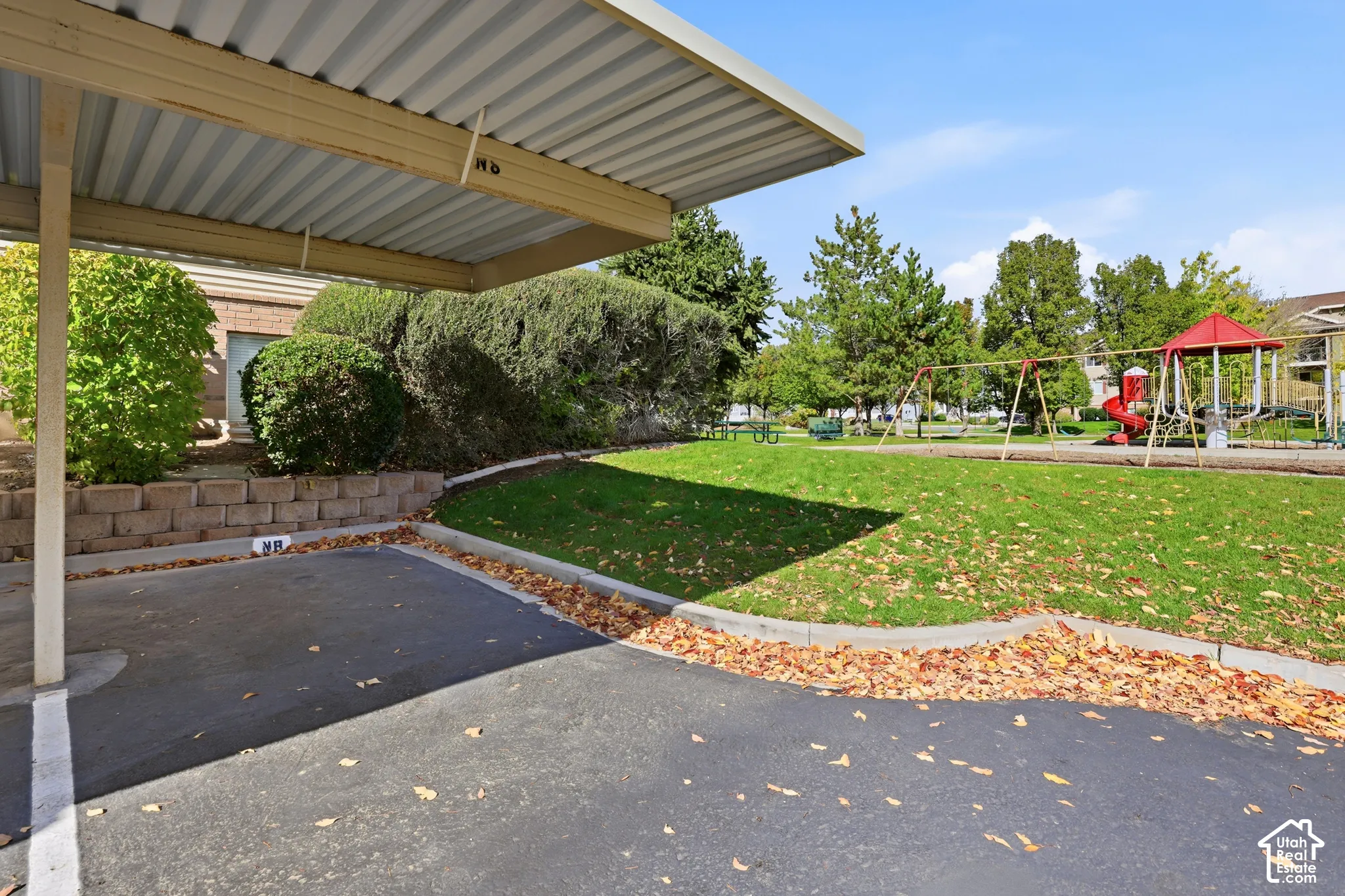 Covered parking space featuring a metal canopy, concrete retaining wall, manicured lawn area, and playground structure