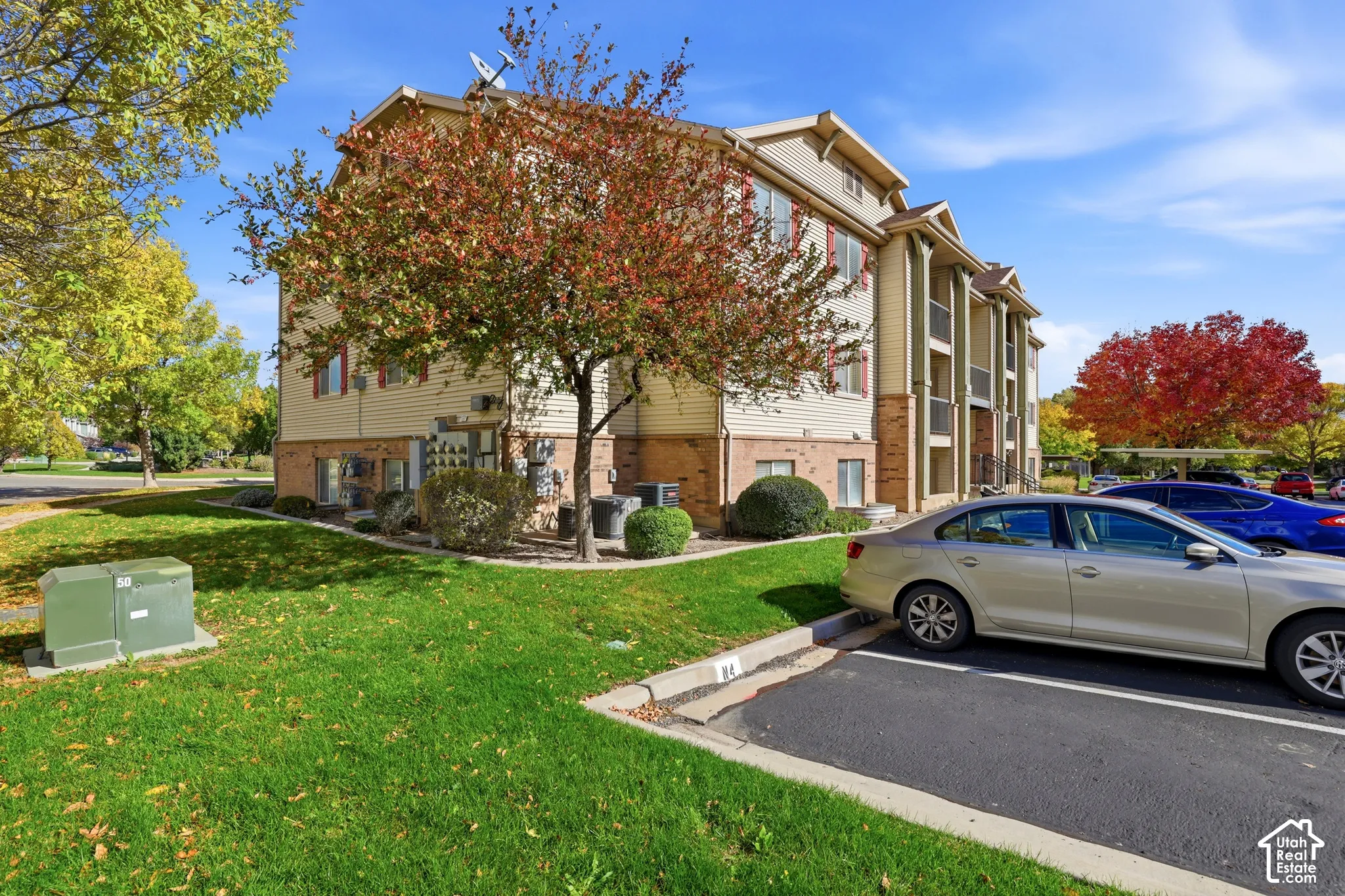 Multi-story building exterior featuring vinyl siding, brick masonry detailing, covered balconies, and paved surface parking