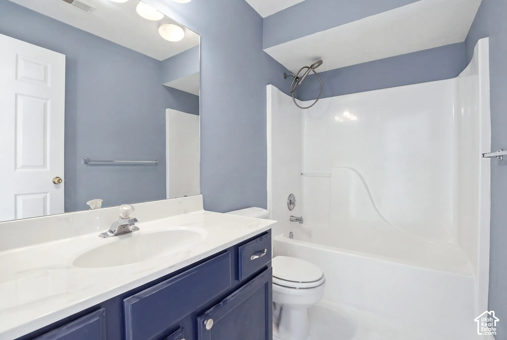 Bathroom featuring a navy vanity cabinet, integrated sink countertop, wall-mounted mirror, and a white acrylic tub-shower combination with a handheld showerhead