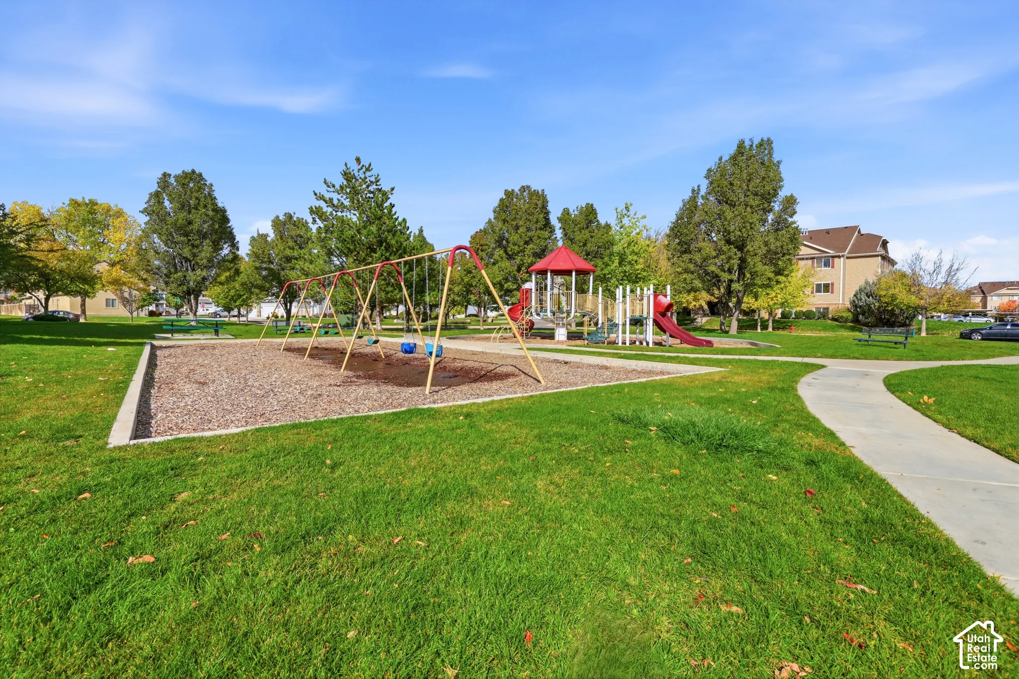 Community grounds featuring a playground, swing set, concrete walking paths, and mature trees