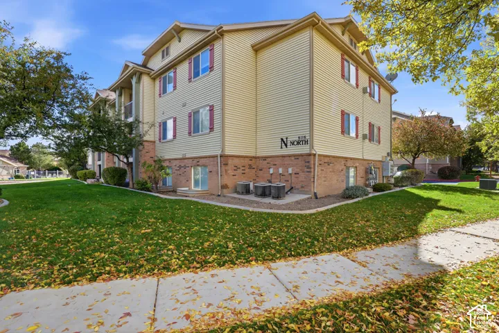 Three-story building exterior featuring vinyl siding, brick veneer foundation, decorative shutters, and gabled rooflines
