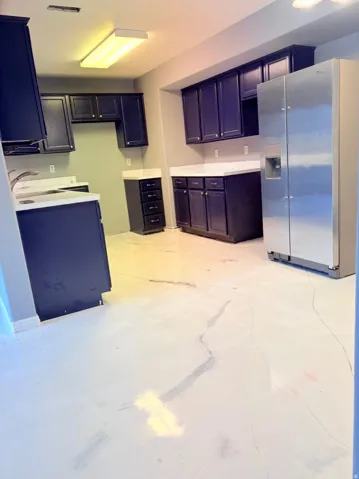 Kitchen with stainless steel fridge with ice dispenser, light countertops, and concrete flooring