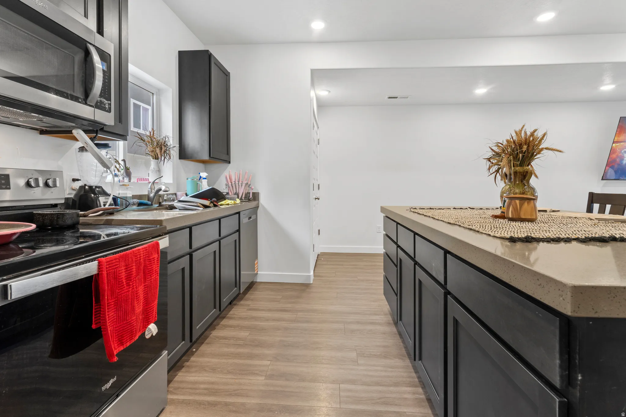 Kitchen featuring stainless steel appliances, dark cabinets, light wood-type flooring, recessed lighting, and dark stone counters