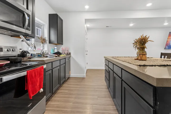 Kitchen featuring stainless steel appliances, dark cabinets, light wood-type flooring, recessed lighting, and dark stone counters