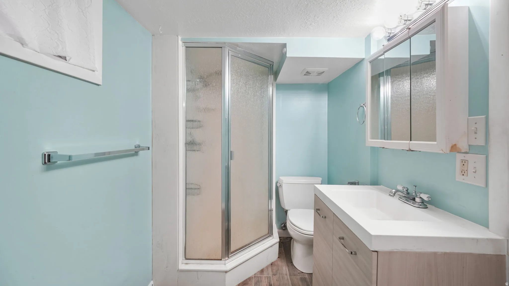 Bathroom with vanity, a shower stall, a textured ceiling, and dark wood-type flooring
