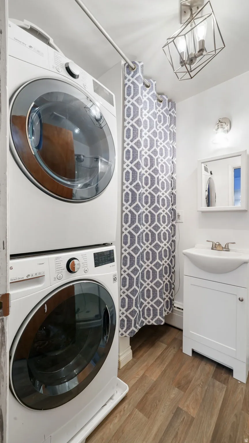 Laundry area with wood finished floors, stacked washer / dryer, a chandelier, and a baseboard radiator
