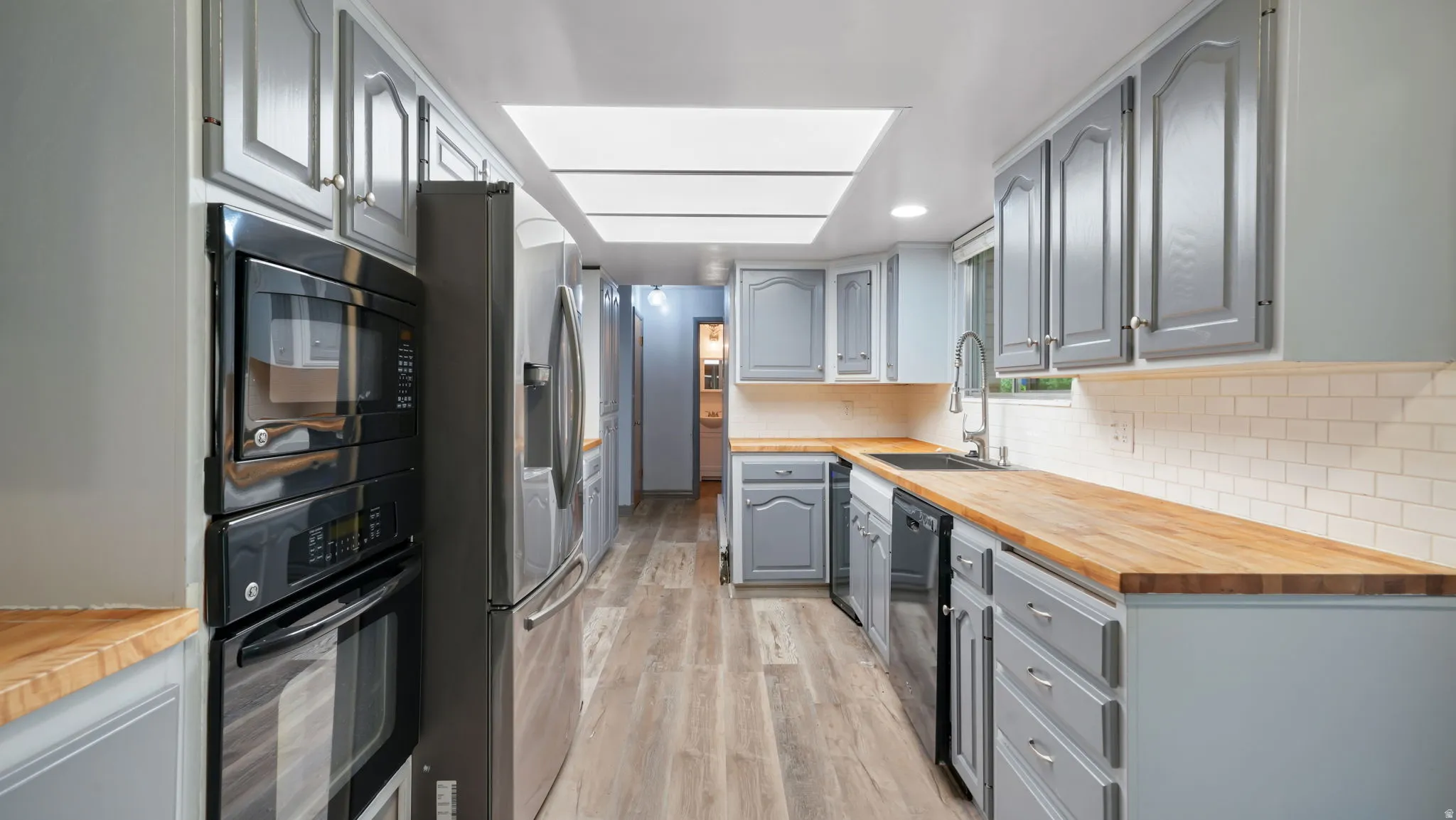 Kitchen featuring wooden counters, gray cabinets, black appliances, light wood finished floors, and tasteful backsplash