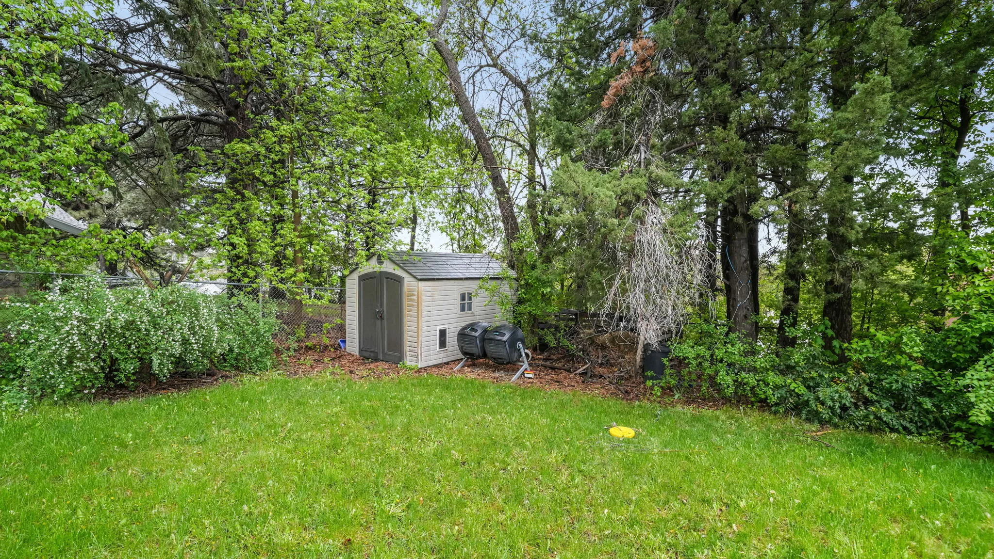 Fenced yard with a storage unit and view of wooded area