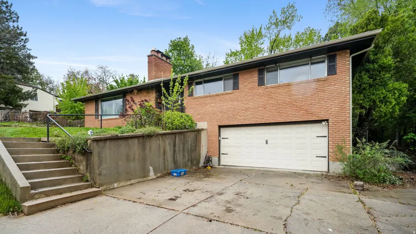 View of front of home featuring a chimney, concrete driveway, an attached garage, and brick siding