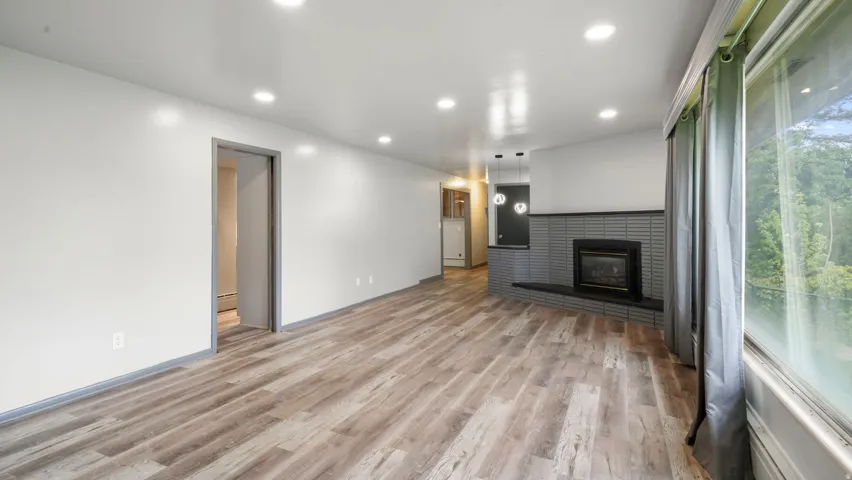 Unfurnished living room with light wood-style floors, recessed lighting, a brick fireplace, and baseboard heating