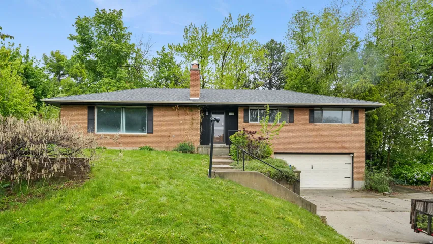 Single story home featuring an attached garage, a front lawn, brick siding, concrete driveway, and a chimney