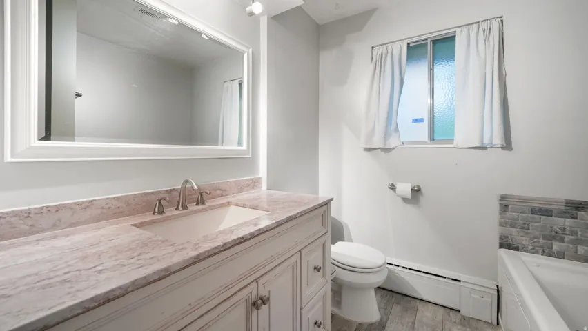 Full bath featuring a baseboard heating unit, vanity, light wood-style flooring, and a garden tub