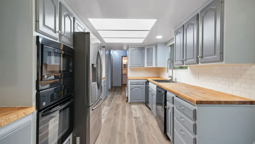 Kitchen featuring wooden counters, gray cabinets, black appliances, light wood finished floors, and tasteful backsplash