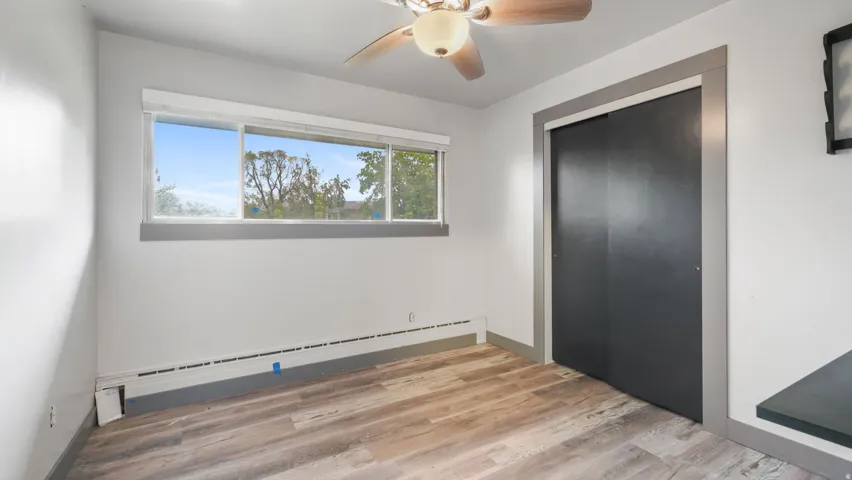 Unfurnished bedroom with a baseboard radiator, light wood-type flooring, ceiling fan, and a closet