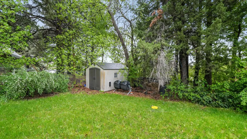 Fenced yard with a storage unit and view of wooded area