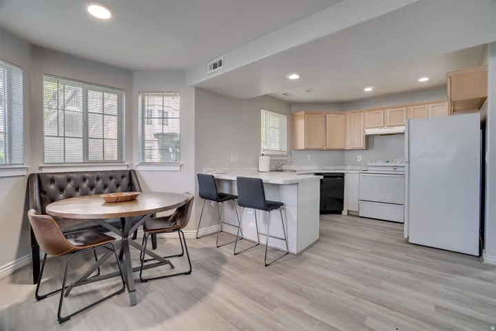 Kitchen with light countertops, white appliances, a kitchen bar, light wood finish cabinets, and a peninsula