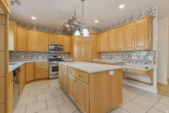 Kitchen featuring light tile patterned floors, a center island, stainless steel appliances, and light wood finish cabinetry