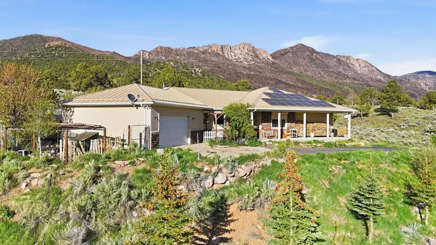 Ranch-style house featuring a mountain view, solar panels, an attached garage, stone siding, and stucco siding