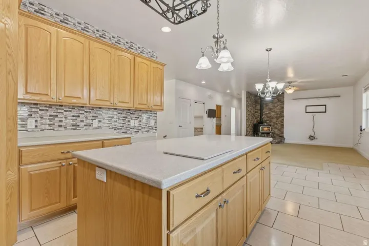 Kitchen featuring a kitchen island, light wood finish cabinetry, light countertops, hanging lights, and a wood stove
