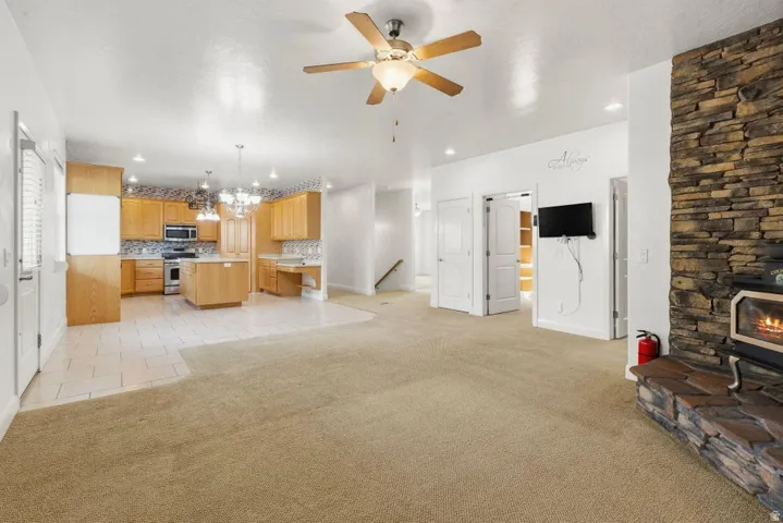 Living room with light carpet, suspended lighting, ceiling fan, and a wood stove