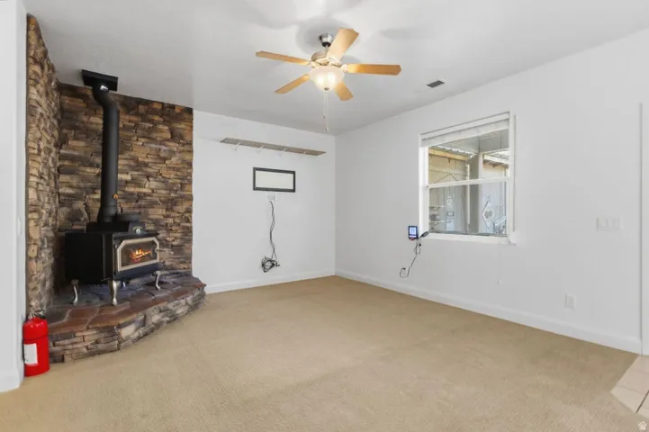 Unfurnished living room featuring a wood stove, ceiling fan, and light carpet