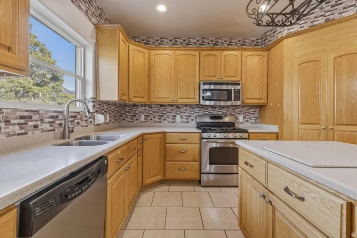 Kitchen with stainless steel appliances, light tile patterned floors, light wood finish cabinets, light stone countertops, and decorative backsplash
