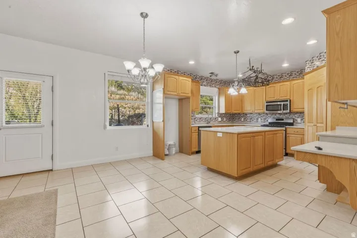 Kitchen featuring hanging lights, a center island, light countertops, decorative backsplash, and stainless steel appliances