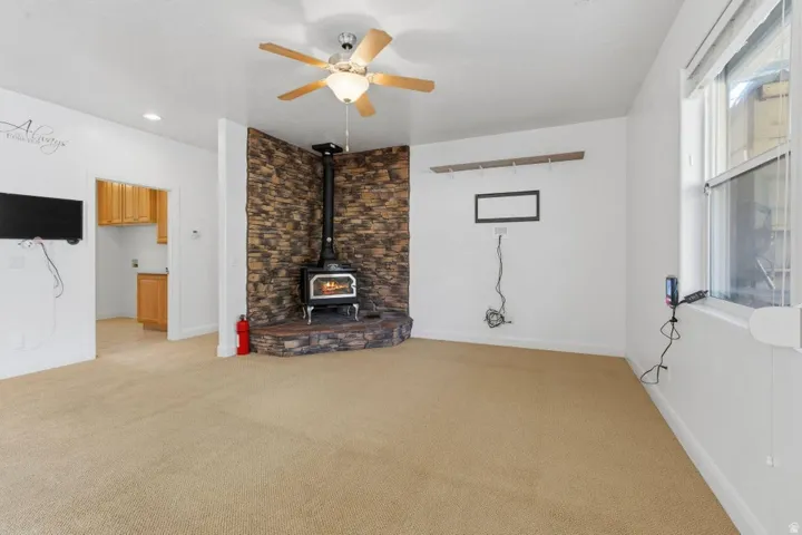 Unfurnished living room with ceiling fan, light carpet, and a wood stove