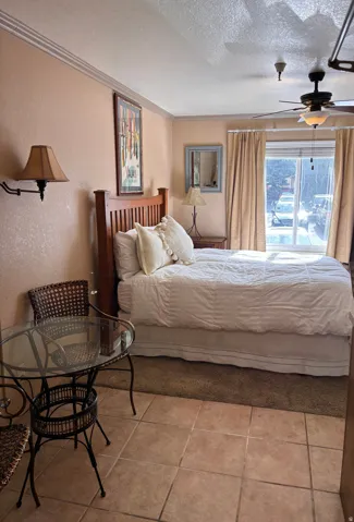 Bedroom featuring a textured ceiling, a textured wall, crown molding, a ceiling fan, and light tile patterned floors