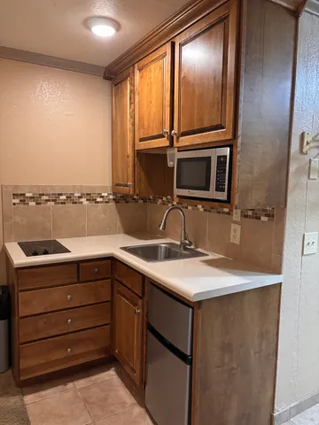 Kitchen with a textured wall, tasteful backsplash, light countertops, stainless steel appliances, and wood finish cabinets