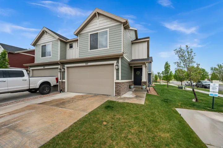 View of front of property featuring an attached garage, concrete driveway, stone siding, and a front lawn